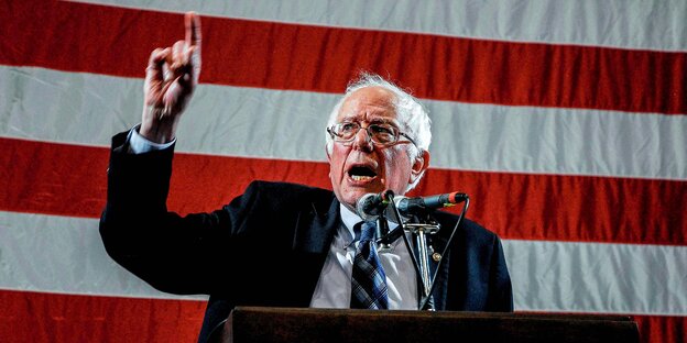 Bernie Sanders steht vor der US-Flagge an einem Pult und redet Bernie Sanders steht vor der US-Flagge an einem Pult und redet