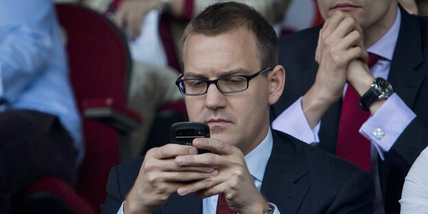 Ein Mann benutzt sein Handy auf der Tribüne bei einem Fußballspiel Ein Mann benutzt sein Handy auf der Tribüne bei einem Fußballspiel