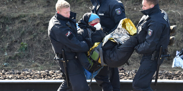 Polizisten tragen Demonstranten neben einem Gleisbett