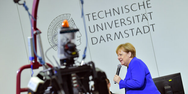Merkel steht in veilchenblauem Jacket vor einem Roboter Merkel steht in veilchenblauem Jacket vor einem Roboter