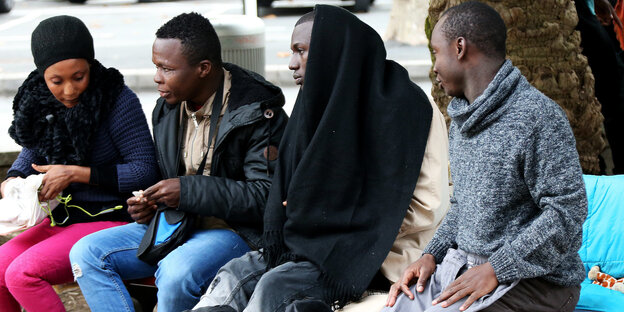 Migranten sitzen auf einer Bank an einem Platz in Bayonne Migranten sitzen auf einer Bank an einem Platz in Bayonne