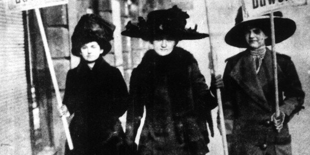 Drei Frauen laufen die Straße entlag und halten Schilder, auf denen sie zum Wählen auffordern Drei Frauen laufen die Straße entlag und halten Schilder, auf denen sie zum Wählen auffordern