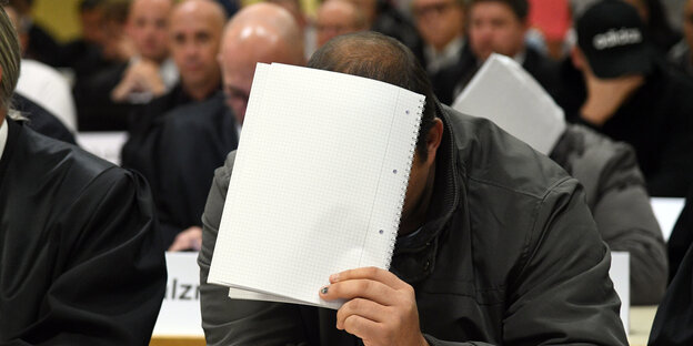 Ein Angeklagter hält ein Blatt Papier vor sein Gesicht Ein Angeklagter hält ein Blatt Papier vor sein Gesicht