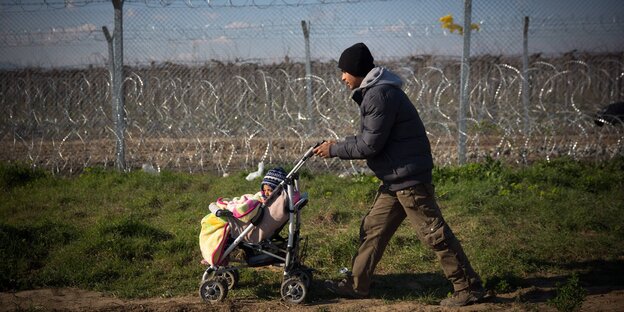 Ein Mann schiebt einen Kinderwagen. Hinter ihm ist ein Stacheldrahtzaun zu sehen Ein Mann schiebt einen Kinderwagen. Hinter ihm ist ein Stacheldrahtzaun zu sehen