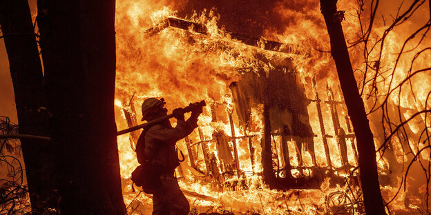 Ein Feuerwehrmann vor einem brennenden Haus Ein Feuerwehrmann vor einem brennenden Haus