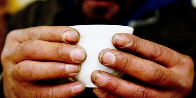 Ein Mann mit schmutzigen Fingern hält eine Tasse.