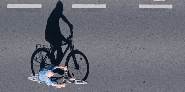 Ein Fahrradfahrer, der einen großen Schatten wirft, aus der Vogelperspektive aufgenommen Ein Fahrradfahrer, der einen großen Schatten wirft, aus der Vogelperspektive aufgenommen