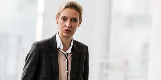 Alice Weidel steht vor einem hellen Hintergrund und schaut ernst