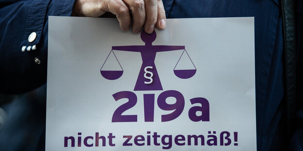 Eine Frau hält einen Zettel mit der Aufschrift "219a nicht zeitgemäß"