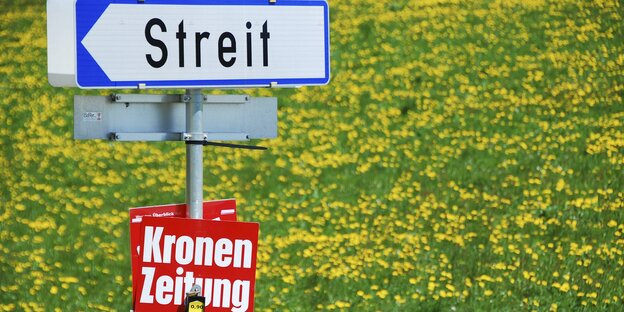 Auf einer Blumenwiese ist ein Zeitungsständer der Kronen Zeitung zu sehen, darüber ein Ortsschild nach Streit Auf einer Blumenwiese ist ein Zeitungsständer der Kronen Zeitung zu sehen, darüber ein Ortsschild nach Streit