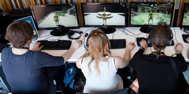 Frauen und Männer sitzen mit Kopfhörern vor Computern und spielen ein Videospiel Frauen und Männer sitzen mit Kopfhörern vor Computern und spielen ein Videospiel