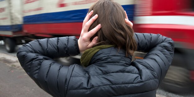 Eine Frau steht an einer Straße und hält sich die Ohren zu. Eine Frau steht an einer Straße und hält sich die Ohren zu.
