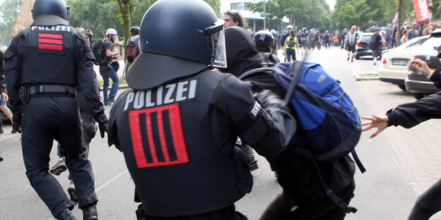 Ein Polizist schlägt mit einem Schlagstock auf einen schwarzgekleideten Demonstranten Ein Polizist schlägt mit einem Schlagstock auf einen schwarzgekleideten Demonstranten