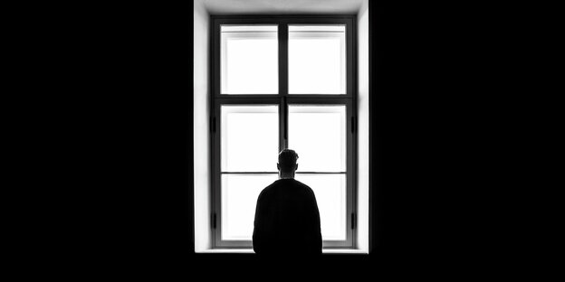Eine Person steht einsam vor einem Fenster. Den Rücken hat sie dem Betrachter zugewandt Eine Person steht einsam vor einem Fenster. Den Rücken hat sie dem Betrachter zugewandt