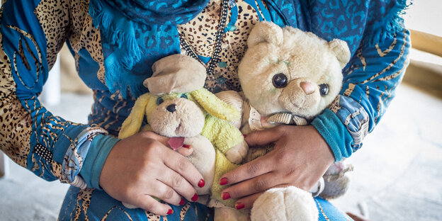 Ein Mädchen klammert sich an Kuscheltiere, sein Kopf ist nicht im Bild zu sehen Ein Mädchen klammert sich an Kuscheltiere, sein Kopf ist nicht im Bild zu sehen