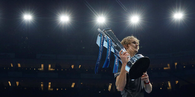 Der Tennisspieler Alexander Zverev steht mit seinem Pokal in einer Arena Der Tennisspieler Alexander Zverev steht mit seinem Pokal in einer Arena