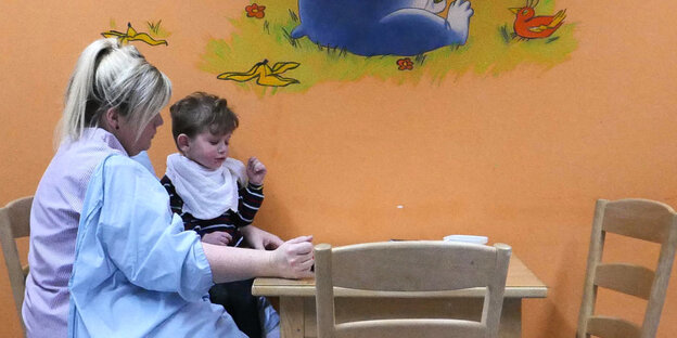 Eine Frau sitzt mit einem Kind auf dem Schoß an einem Tisch Eine Frau sitzt mit einem Kind auf dem Schoß an einem Tisch