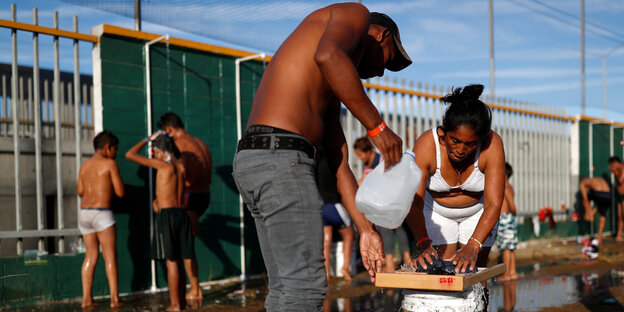 Flüchtlingslager in Tijuana: eine Frau und ein Mann waschen Wäsche, dahinter duschen andere Menschen