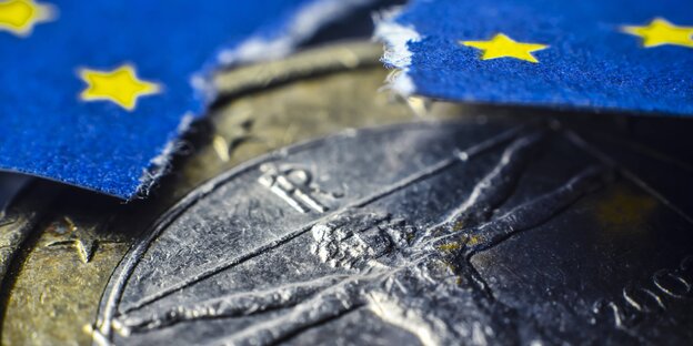 Eine Euromünze, darüber eine eingerissen Europaflagge Eine Euromünze, darüber eine eingerissen Europaflagge