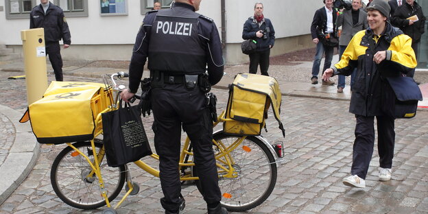 Ein Polizeibeamter legt Hand am Fahrrad einer Postzustellerin an. Ein Polizeibeamter legt Hand am Fahrrad einer Postzustellerin an.