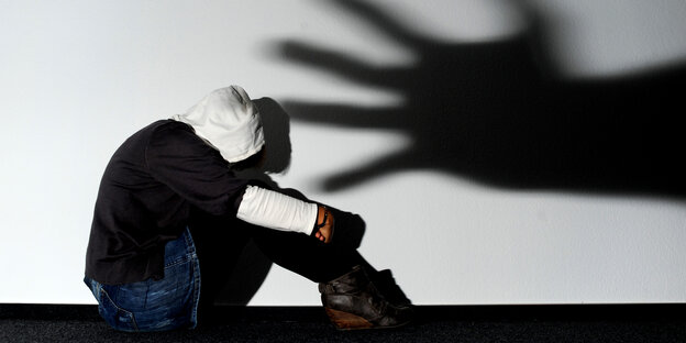 Ein Mädchen sitzt vor einer Wand in Hannover, auf der der Schatten einer Hand groß zu sehen ist Ein Mädchen sitzt vor einer Wand in Hannover, auf der der Schatten einer Hand groß zu sehen ist