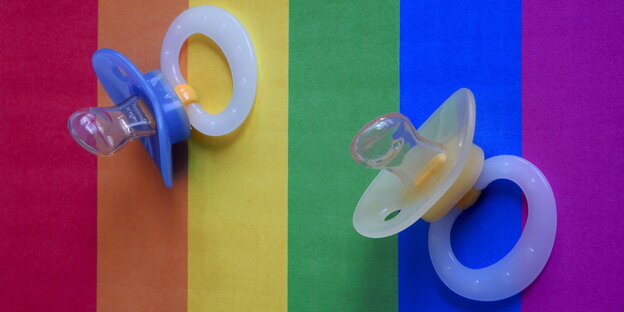 Auf einer Regenbogenfahne liegen zwei Schnuller Auf einer Regenbogenfahne liegen zwei Schnuller