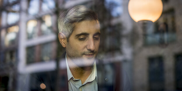 Michel Abdollahi durch eine Fensterscheibe mit Spiegelungen gesehen Michel Abdollahi durch eine Fensterscheibe mit Spiegelungen gesehen