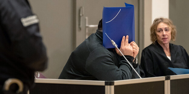 NIels Högel hält sich einen Aktendeckel vors Gesicht. NIels Högel hält sich einen Aktendeckel vors Gesicht.