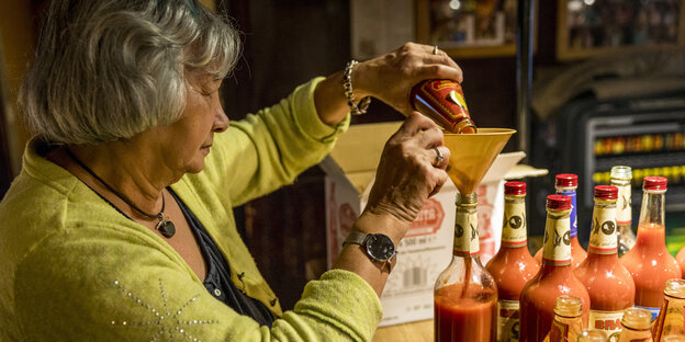 Eine Frau gießt Tomatensaft durch einen Trichter Eine Frau gießt Tomatensaft durch einen Trichter