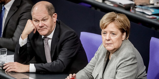 Ein Mann und eine Frau, Olaf Scholz und Angela Merkel, sitzen in Anzügen nebeneinander Ein Mann und eine Frau, Olaf Scholz und Angela Merkel, sitzen in Anzügen nebeneinander