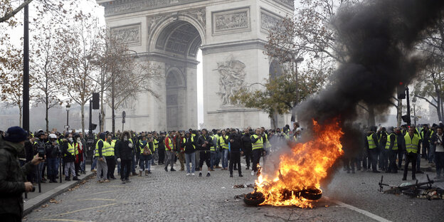Demonstranten in gelben Westen scharen sich um einen brennenden Gegenstand in Paris Demonstranten in gelben Westen scharen sich um einen brennenden Gegenstand in Paris