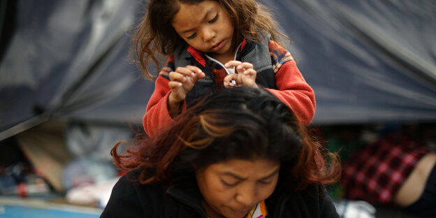 Ein kleines Mädchen sitzt auf den Schultern ihrer Mutter in einer Flüchtlingsunterkunft im mexikanischen Tijuana Ein kleines Mädchen sitzt auf den Schultern ihrer Mutter in einer Flüchtlingsunterkunft im mexikanischen Tijuana