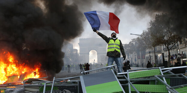 Ein Mann in einer gelben Warnweste steht neben eine brennenden Barrikade vor dem Triumphbogen in Paris Ein Mann in einer gelben Warnweste steht neben eine brennenden Barrikade vor dem Triumphbogen in Paris