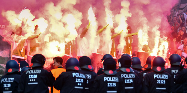 Brennende bengalische Feuer im Stadion, davor stehen Polizisten Brennende bengalische Feuer im Stadion, davor stehen Polizisten