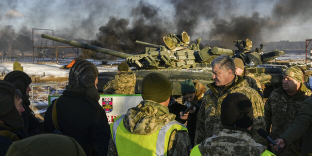 Ein Mann, Petro Poroschenko, spricht mit einer Gruppe von Soldaten, im Hintergrund ein Militärpanzer und viele dunkle Rauchschwaden Ein Mann, Petro Poroschenko, spricht mit einer Gruppe von Soldaten, im Hintergrund ein Militärpanzer und viele dunkle Rauchschwaden