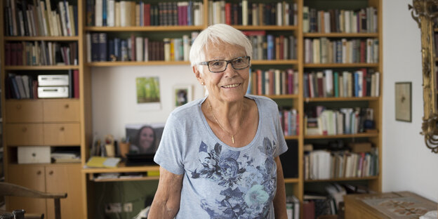 Eine ältere Frau vor einem Bücherregal blickt in die Kamera Eine ältere Frau vor einem Bücherregal blickt in die Kamera
