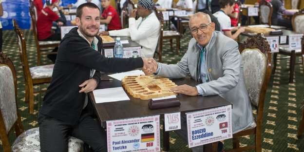 Zwei Männer reichen sich über einem Brettspiel die Hand Zwei Männer reichen sich über einem Brettspiel die Hand