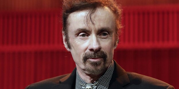 T. C. Boyle trägt einen Anzug und ist vor einer roten Wand zu sehen T. C. Boyle trägt einen Anzug und ist vor einer roten Wand zu sehen