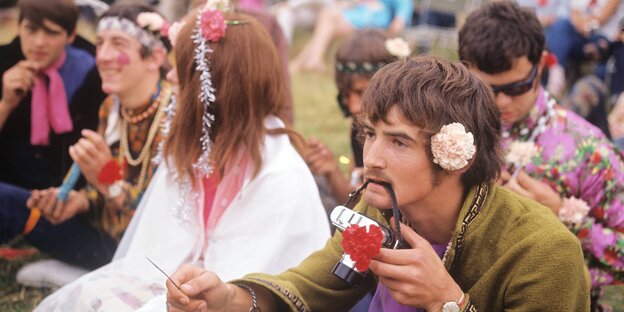 Auf einer Wiese sitzen bunt gekleidete Menschen mit Blumen in den Haaren Auf einer Wiese sitzen bunt gekleidete Menschen mit Blumen in den Haaren