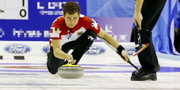 Ein junger Mann, Marc Muskatewitz, spielt konzentriert Curling auf einer Eisfläche Ein junger Mann, Marc Muskatewitz, spielt konzentriert Curling auf einer Eisfläche