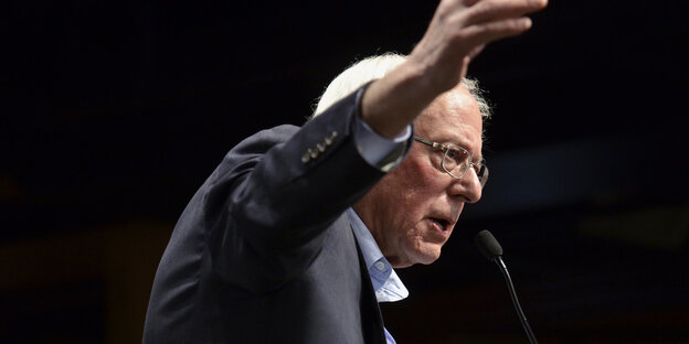 Bernie Sanders breitet vor schwarzem Hintergrund drohend beide Arme aus Bernie Sanders breitet vor schwarzem Hintergrund drohend beide Arme aus