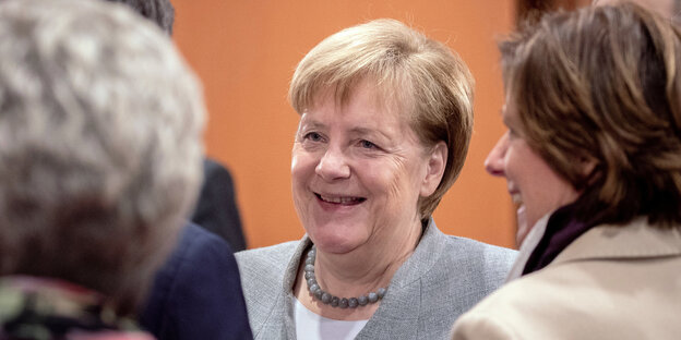 Angela Merkel lächelt, umgeben von anderen Personen Angela Merkel lächelt, umgeben von anderen Personen