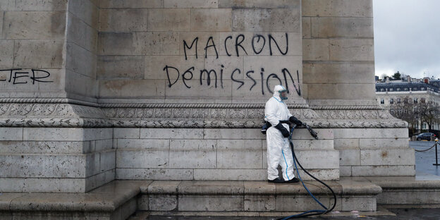 Ein Mann in weißem Schutzanzug vor einem Graffito "Macron Demission" Ein Mann in weißem Schutzanzug vor einem Graffito "Macron Demission"