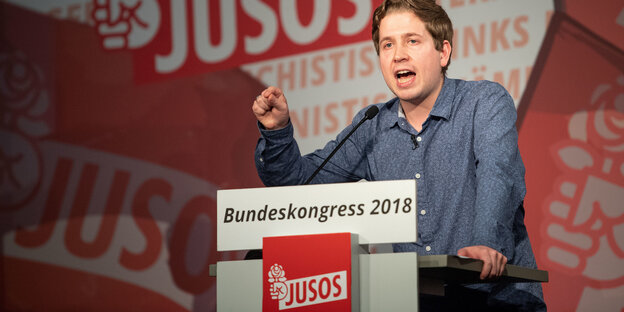 Kevin Kühnert an einem Rednerpult, mit geballter Faust, hinter ihm der Juso-Schriftzug Kevin Kühnert an einem Rednerpult, mit geballter Faust, hinter ihm der Juso-Schriftzug