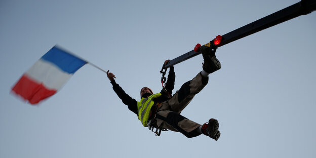 Ein Mann in gelber Weste hängt an einem Kran und schwenkt dabei eine französische Flagge