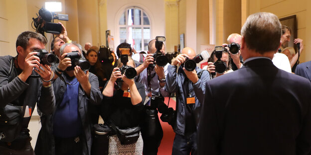 Ein Mann steht mit dem Rücken zum Betrachter und wird von vielen Fotografen abgelichtet