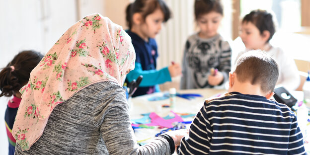 Ein Frau mit Kopftuch sitzt mit Kindern an einem Tisch und bastelt.