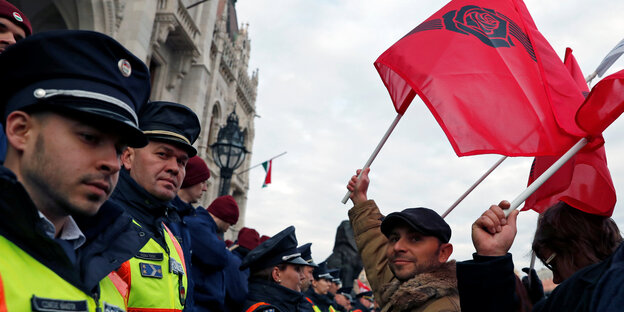 Ein Mann steht neben zwei Polizisten und hält eine rote Flagge in die Luft Ein Mann steht neben zwei Polizisten und hält eine rote Flagge in die Luft