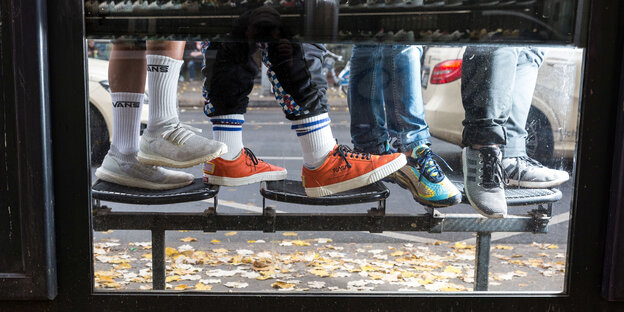 Durch ein Fenster einer Busstation sieht man die Schuhe von fünf Menschen. Durch ein Fenster einer Busstation sieht man die Schuhe von fünf Menschen.