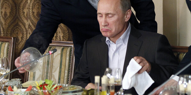 Putin sitzt alleine an einem Konferenztisch, vor ihm steht essen Putin sitzt alleine an einem Konferenztisch, vor ihm steht essen